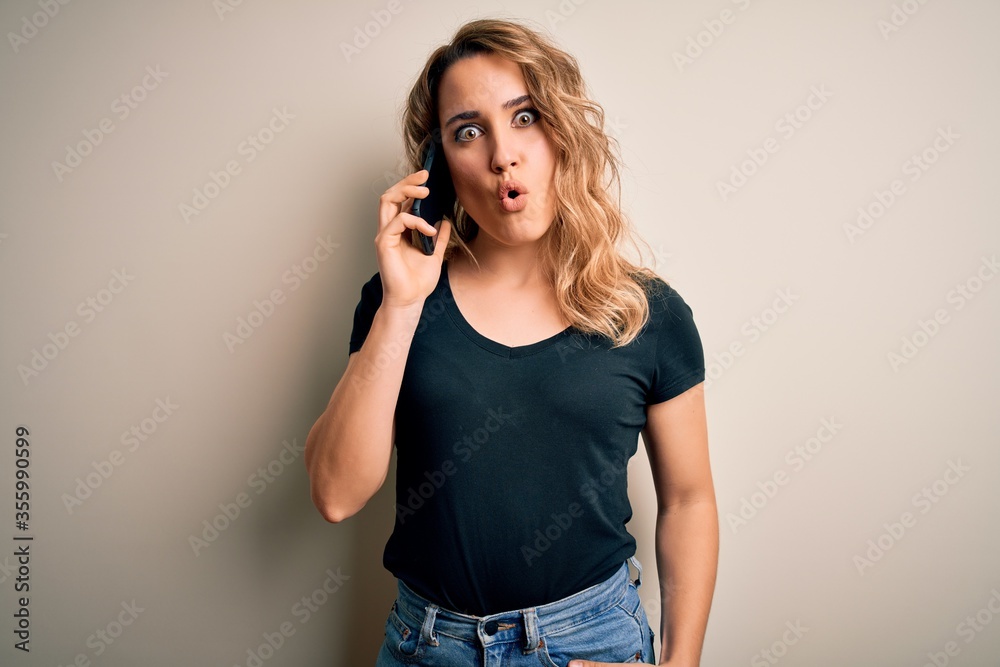 Beautiful blonde woman having conversation talking on the smartphone over white background scared in shock with a surprise face, afraid and excited with fear expression Beautiful blonde woman having conversation talking on the smartphone over white background scared in shock with a surprise face, afraid and excited with fear expression