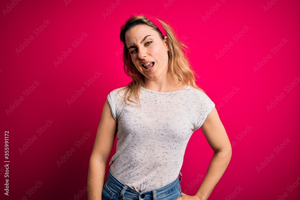 Young beautiful blonde woman wearing casual t-shirt standing over isolated pink background winking looking at the camera with sexy expression, cheerful and happy face.
