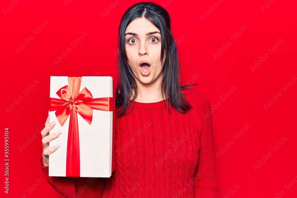 Young beautiful girl holding gift scared and amazed with open mouth for surprise, disbelief face Young beautiful girl holding gift scared and amazed with open mouth for surprise, disbelief face