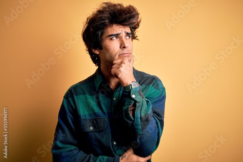 Young handsome man wearing casual shirt standing over isolated yellow background Thinking worried about a question, concerned and nervous with hand on chin © Krakenimages.com