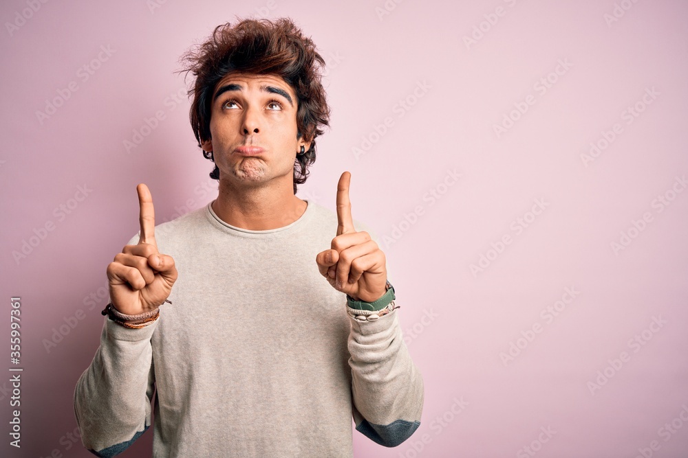 Young handsome man wearing casual t-shirt standing over isolated pink background Pointing up looking sad and upset, indicating direction with fingers, unhappy and depressed. Young handsome man wearing casual t-shirt standing over isolated pink background Pointing up looking sad and upset, indicating direction with fingers, unhappy and depressed.