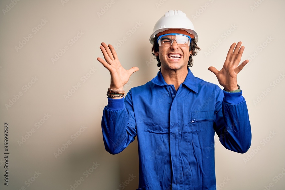 Young constructor man wearing uniform and security helmet over isolated white background celebrating mad and crazy for success with arms raised and closed eyes screaming excited. Winner concept Young constructor man wearing uniform and security helmet over isolated white background celebrating mad and crazy for success with arms raised and closed eyes screaming excited. Winner concept