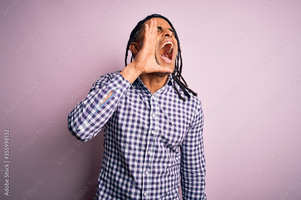 Young handsome african american afro man with dreadlocks wearing casual shirt shouting and screaming loud to side with hand on mouth. Communication concept. Young handsome african american afro man with dreadlocks wearing casual shirt shouting and screaming loud to side with hand on mouth. Communication concept.