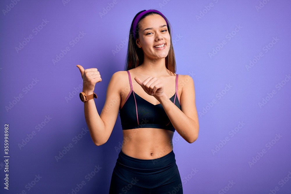 Obraz premium Young beautiful sporty girl doing sport wearing sportswear over isolated purple background Pointing to the back behind with hand and thumbs up, smiling confident