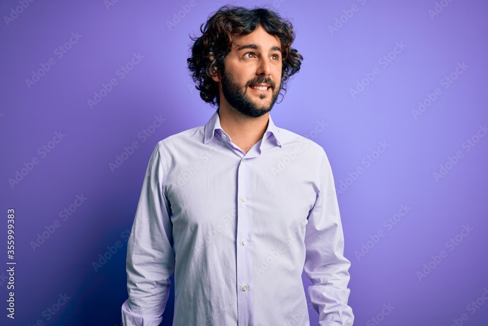 Fototapeta premium Young handsome business man with beard wearing shirt standing over purple background smiling looking to the side and staring away thinking.