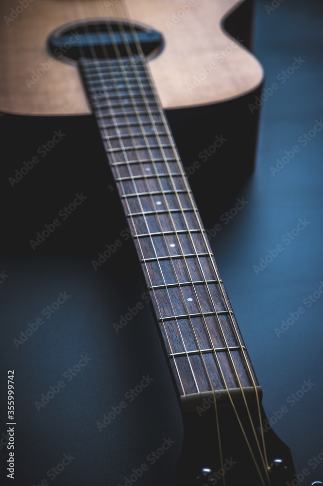 Fototapeta premium Acoustic guitar, music instrument resting against a dark black background with copy space, Close-up of wooden classic guitar