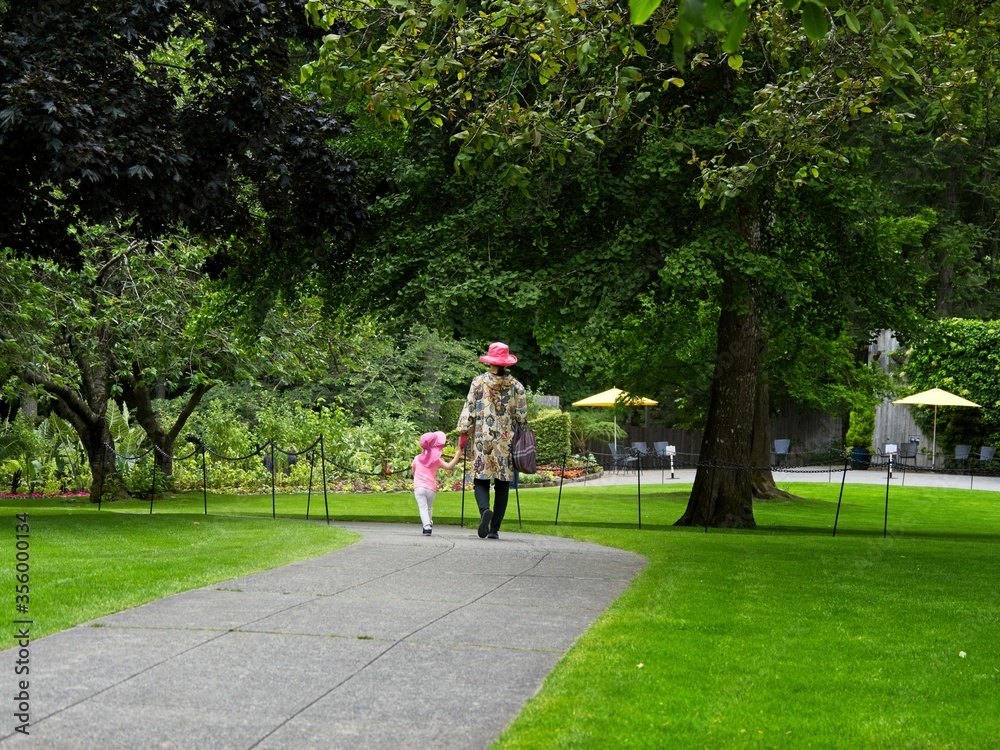 Mother and daughter walk the paved walkway in the springtime garden among the lawns and trees Mother and daughter walk the paved walkway in the springtime garden among the lawns and trees