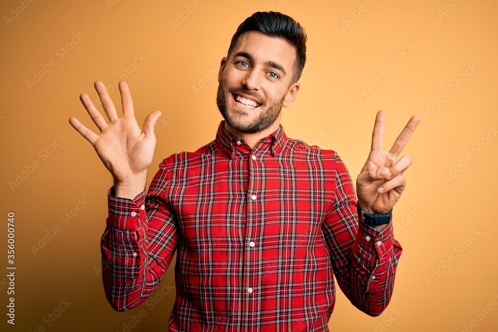Naklejka premium Young handsome man wearing casual shirt standing over isolated yellow background showing and pointing up with fingers number seven while smiling confident and happy.