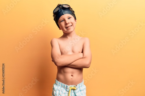 Cute blond kid wearing swimwear and swimmer glasses happy face smiling with crossed arms looking at the camera. positive person. © Krakenimages.com