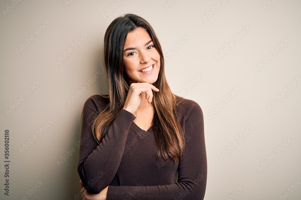 Young beautiful girl wearing casual sweater standing over isolated white background looking confident at the camera with smile with crossed arms and hand raised on chin. Thinking positive. Young beautiful girl wearing casual sweater standing over isolated white background looking confident at the camera with smile with crossed arms and hand raised on chin. Thinking positive.