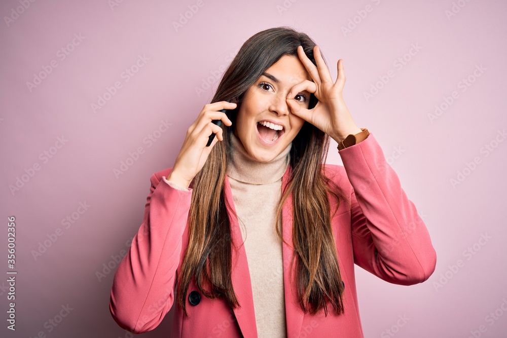 Young beautiful girl having conversation talking on the smartphone over white background with happy face smiling doing ok sign with hand on eye looking through fingers