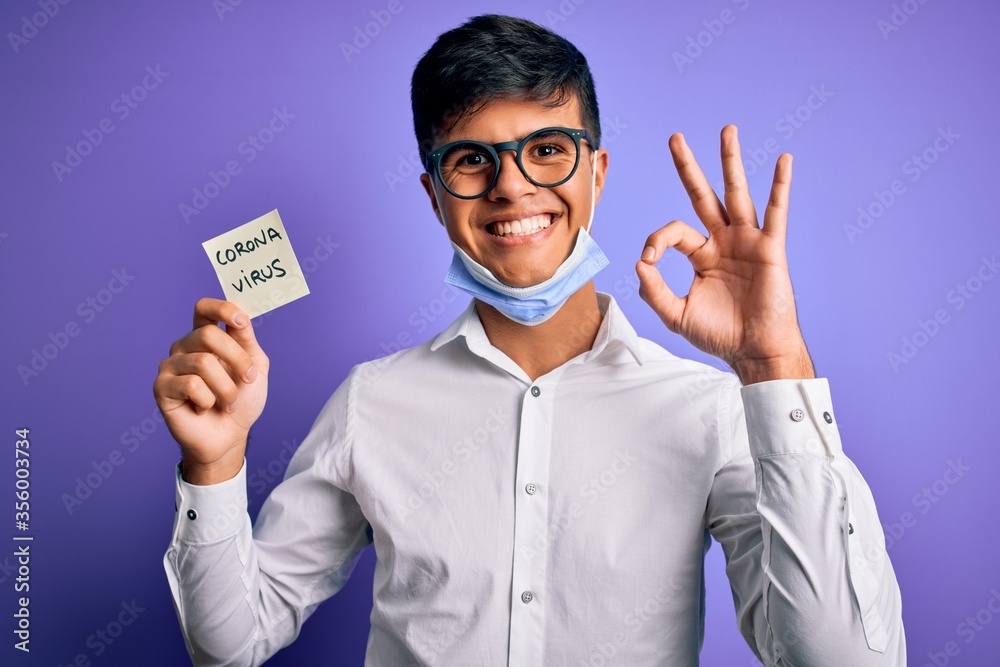 Young handsome man wearing medical mask holding reminder with corona virus message doing ok sign with fingers, excellent symbol Young handsome man wearing medical mask holding reminder with corona virus message doing ok sign with fingers, excellent symbol