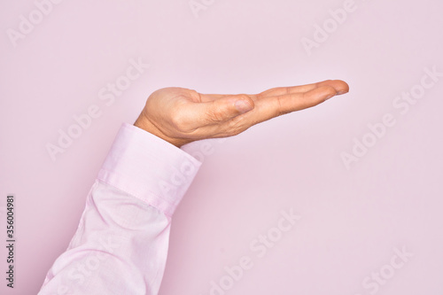 Hand of caucasian young man showing fingers over isolated pink background with flat palm presenting product, offer and giving gesture, blank copy space