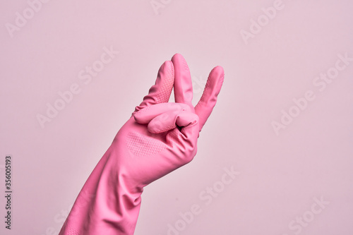 Hand of caucasian young man with cleaning glove over isolated pink background snapping fingers for success, easy and click symbol gesture with hand