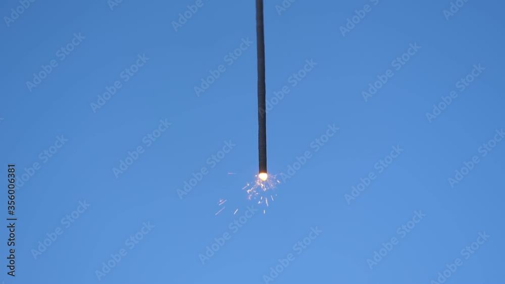 Sparkler hanging in the middle of the frame and burning against blue sky background. Sparkler hanging in the middle of the frame and burning against blue sky background.