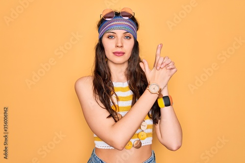 Young beautiful hippie woman with blue eyes wearing accesories and sunnglasses Holding symbolic gun with hand gesture, playing killing shooting weapons, angry face
