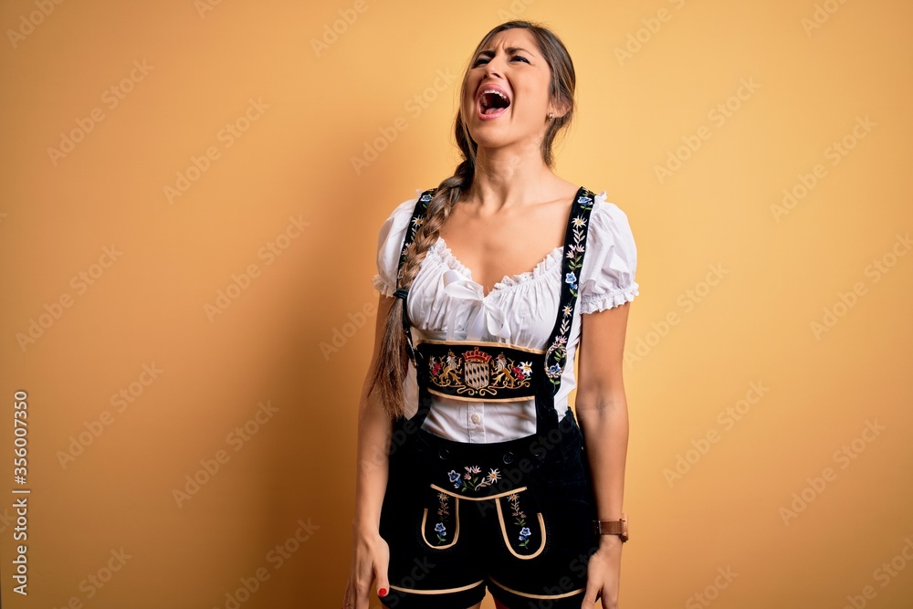 Young beautiful brunette german woman celebrating Octoberfest wearing traditional dress angry and mad screaming frustrated and furious, shouting with anger. Rage and aggressive concept. Young beautiful brunette german woman celebrating Octoberfest wearing traditional dress angry and mad screaming frustrated and furious, shouting with anger. Rage and aggressive concept.
