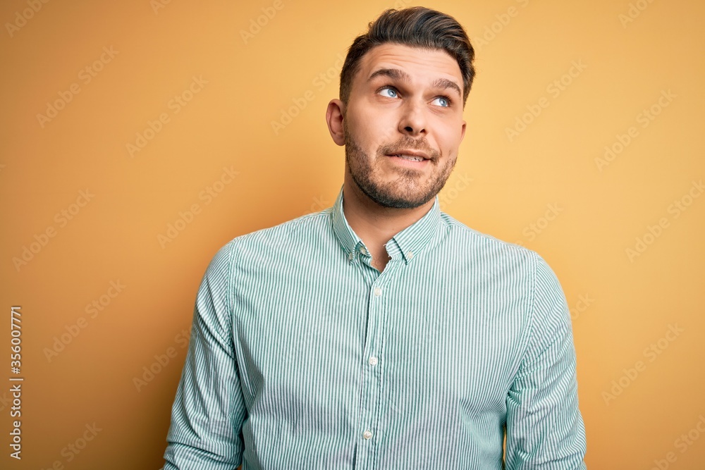 Young business man with blue eyes wearing elegant green shirt over yellow background smiling looking to the side and staring away thinking. Young business man with blue eyes wearing elegant green shirt over yellow background smiling looking to the side and staring away thinking.