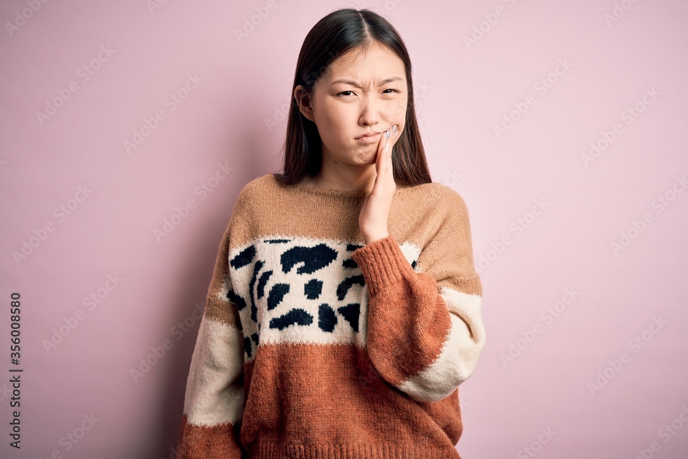 Young beautiful asian woman wearing animal print fashion sweater over pink isolated background touching mouth with hand with painful expression because of toothache or dental illness on teeth. Dentist Young beautiful asian woman wearing animal print fashion sweater over pink isolated background touching mouth with hand with painful expression because of toothache or dental illness on teeth. Dentist