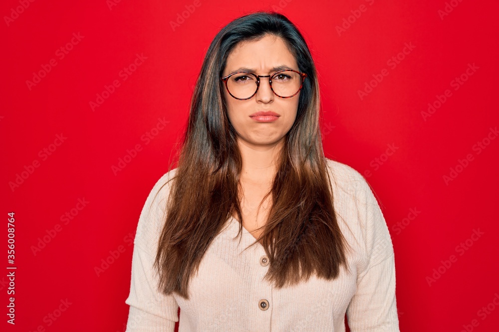 Young hispanic smart woman wearing glasses standing over red isolated background depressed and worry for distress, crying angry and afraid. Sad expression.