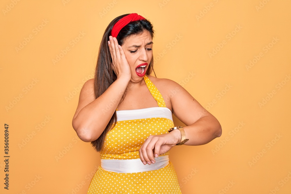 Young hispanic pin up woman wearing fashion sexy 50s style over yellow background Looking at the watch time worried, afraid of getting late Young hispanic pin up woman wearing fashion sexy 50s style over yellow background Looking at the watch time worried, afraid of getting late
