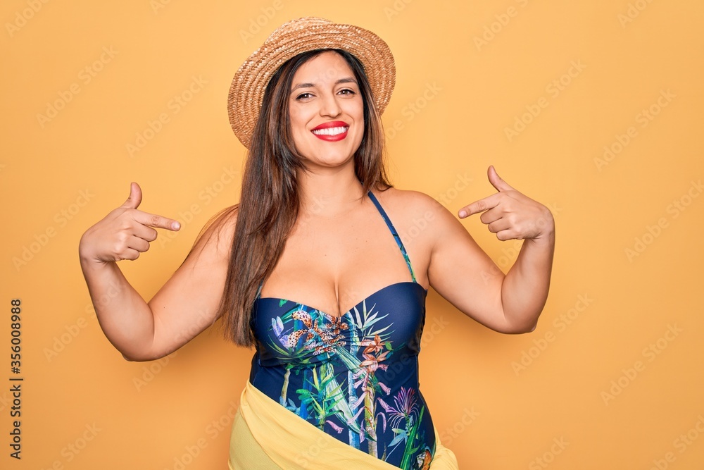 Young hispanic woman wearing summer hat and swimsuit over yellow background looking confident with smile on face, pointing oneself with fingers proud and happy. Young hispanic woman wearing summer hat and swimsuit over yellow background looking confident with smile on face, pointing oneself with fingers proud and happy.