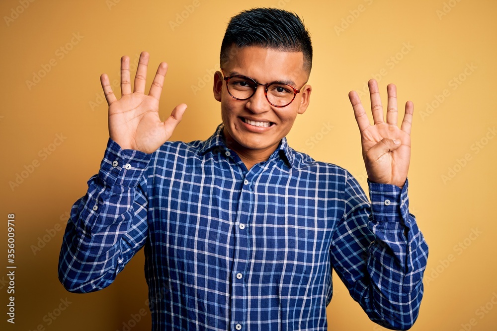 Young handsome latin man wearing casual shirt and glasses over yellow background showing and pointing up with fingers number nine while smiling confident and happy. Young handsome latin man wearing casual shirt and glasses over yellow background showing and pointing up with fingers number nine while smiling confident and happy.