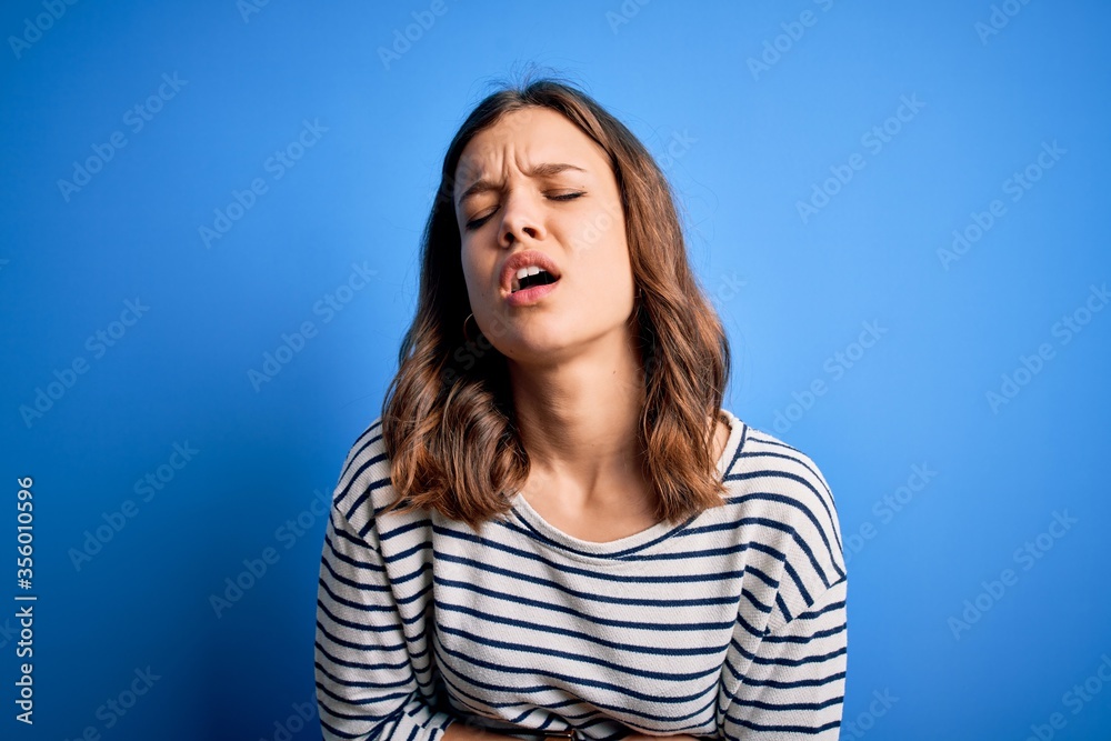 Young beautiful blonde girl wearing casual sweater standing over blue isolated background with hand on stomach because nausea, painful disease feeling unwell. Ache concept. Young beautiful blonde girl wearing casual sweater standing over blue isolated background with hand on stomach because nausea, painful disease feeling unwell. Ache concept.