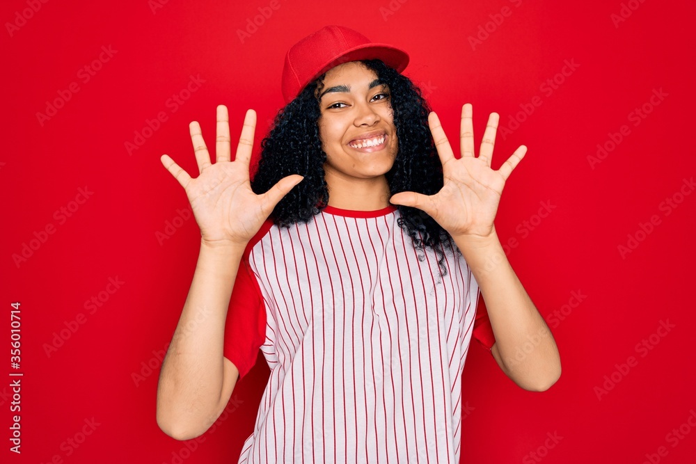 Young african american curly sportswoman wearing baseball cap and striped t-shirt showing and pointing up with fingers number ten while smiling confident and happy. Young african american curly sportswoman wearing baseball cap and striped t-shirt showing and pointing up with fingers number ten while smiling confident and happy.