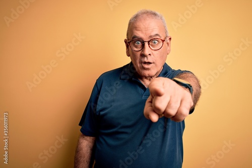Middle age handsome hoary man wearing casual polo and glasses over yellow background pointing displeased and frustrated to the camera, angry and furious with you