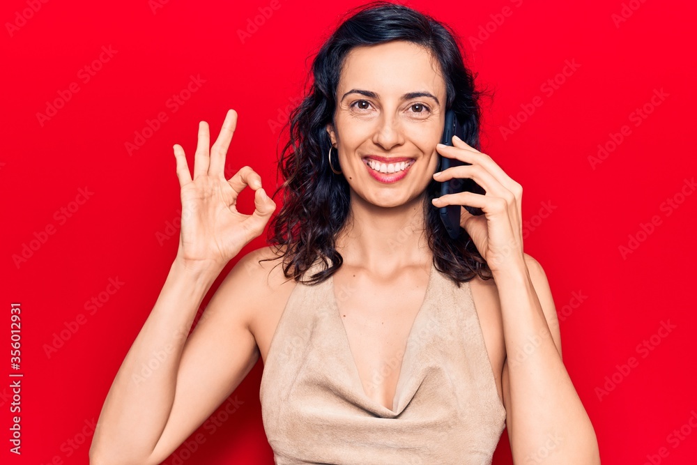 Young beautiful hispanic woman having conversation talking on the smartphone doing ok sign with fingers, smiling friendly gesturing excellent symbol Young beautiful hispanic woman having conversation talking on the smartphone doing ok sign with fingers, smiling friendly gesturing excellent symbol
