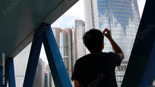 Young asian man in the footbridge looking through his hands up in front of a building seen from his back in Hong Kong International Finance Centre photo