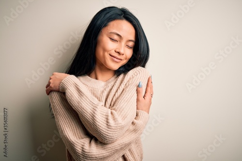 Foto Young beautiful chinese woman wearing casual sweater over isolated white background Hugging oneself happy and positive, smiling confident