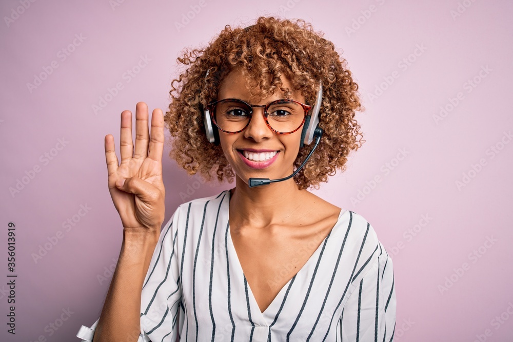 African american curly call center agent woman working using headset over pink background showing and pointing up with fingers number four while smiling confident and happy. African american curly call center agent woman working using headset over pink background showing and pointing up with fingers number four while smiling confident and happy.