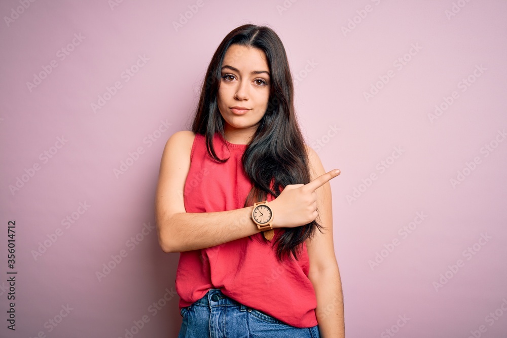 Young brunette woman wearing casual summer shirt over pink isolated background Pointing with hand finger to the side showing advertisement, serious and calm face Young brunette woman wearing casual summer shirt over pink isolated background Pointing with hand finger to the side showing advertisement, serious and calm face