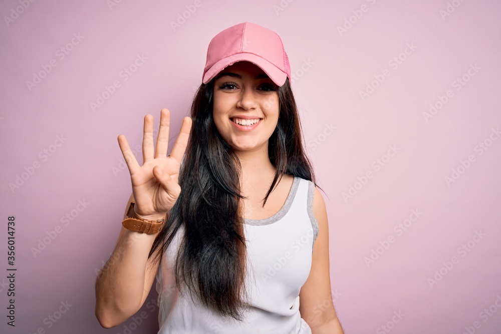 Young brunette woman wearing casual sport cap over pink background showing and pointing up with fingers number four while smiling confident and happy. Young brunette woman wearing casual sport cap over pink background showing and pointing up with fingers number four while smiling confident and happy.