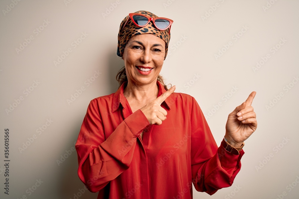 Middle age brunette woman wearing handkerchief on head and shirt over white background smiling and looking at the camera pointing with two hands and fingers to the side.