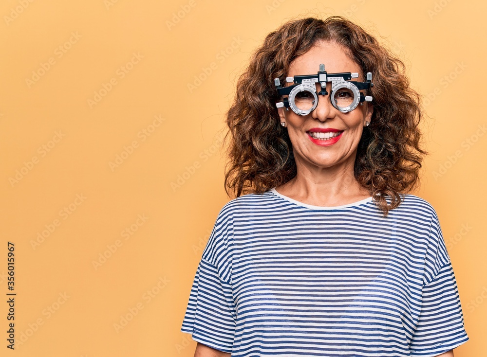 Middle age beautiful woman controlling vision using optometry glasses over yellow background with a happy and cool smile on face. Lucky person. Middle age beautiful woman controlling vision using optometry glasses over yellow background with a happy and cool smile on face. Lucky person.