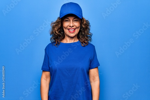 Middle age beautiful delivery woman wearing blue uniform and cap over isolated background with a happy and cool smile on face. Lucky person.