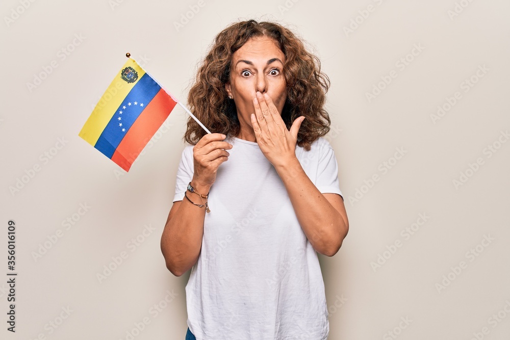 Middle age beautiful tourist woman holding venezuelan flag over isolated white background covering mouth with hand, shocked and afraid for mistake. Surprised expression Middle age beautiful tourist woman holding venezuelan flag over isolated white background covering mouth with hand, shocked and afraid for mistake. Surprised expression