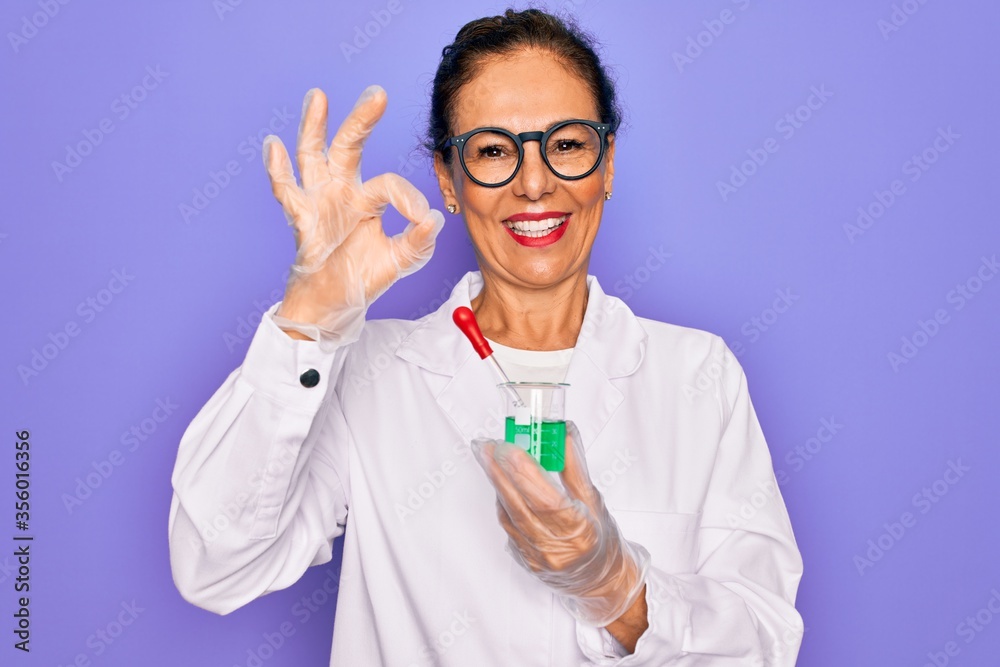 Middle age senior scientist woman wearing laboratory coat holding research test tube doing ok sign with fingers, excellent symbol Middle age senior scientist woman wearing laboratory coat holding research test tube doing ok sign with fingers, excellent symbol