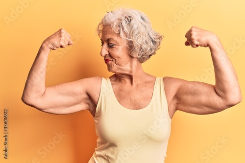 Senior grey-haired woman wearing casual clothes showing arms muscles smiling proud. fitness concept.