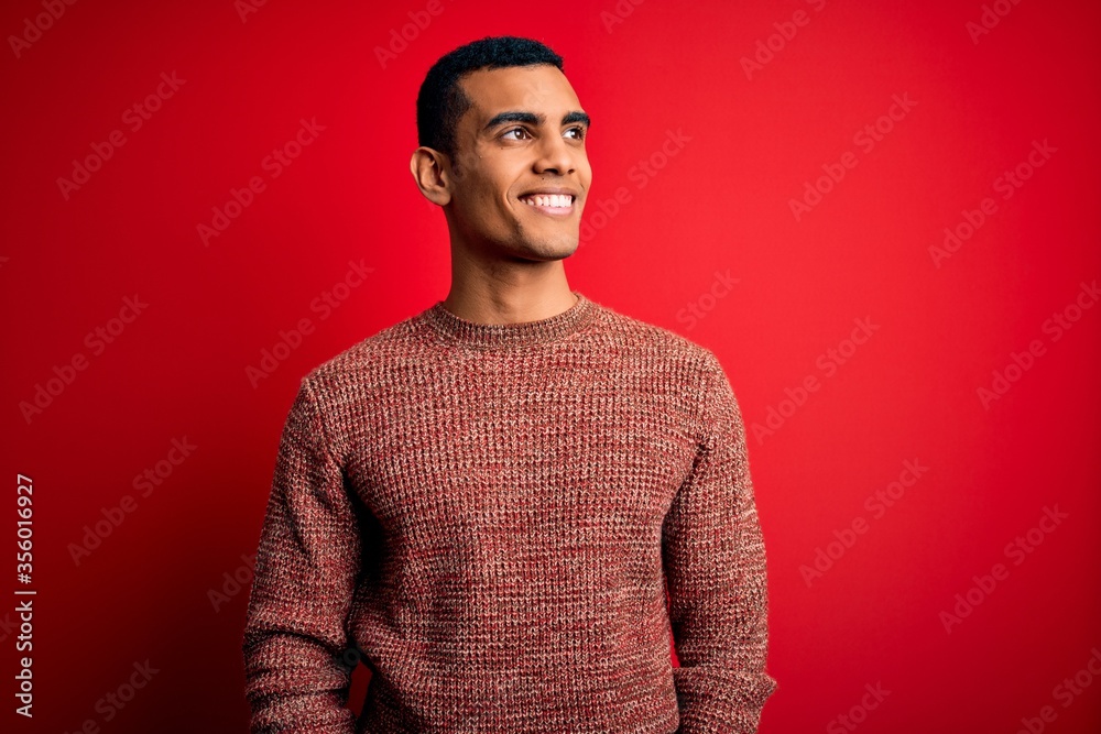Obraz premium Young handsome african american man wearing casual sweater standing over red background looking away to side with smile on face, natural expression. Laughing confident.