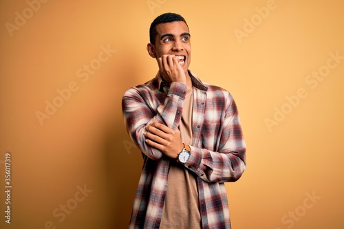 Young handsome african american man wearing casual shirt standing over yellow background looking stressed and nervous with hands on mouth biting nails. Anxiety problem.