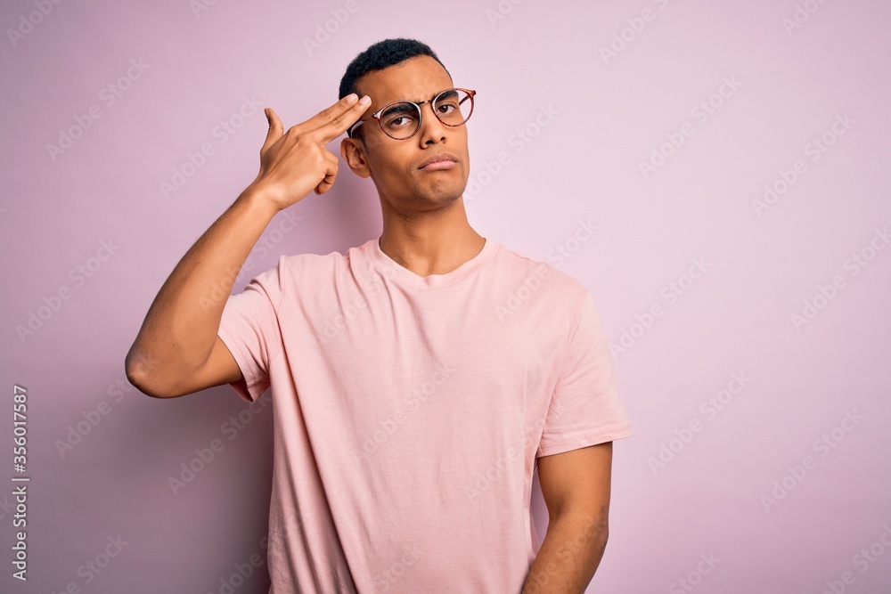 Handsome african american man wearing casual t-shirt and glasses over pink background Shooting and killing oneself pointing hand and fingers to head like gun, suicide gesture.