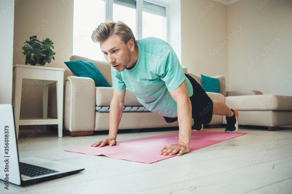 Blonde caucasian man with bristle doing push-ups on the floor using a laptop Blonde caucasian man with bristle doing push-ups on the floor using a laptop