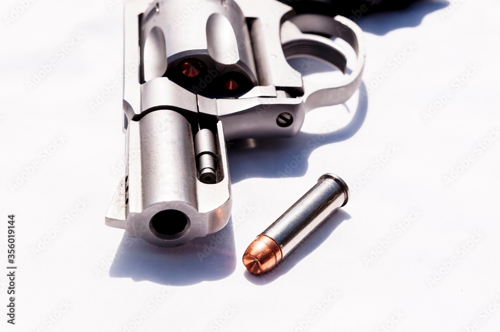 A stainless snub nosed 357 magnum revolver with a hollow point bullet next to it on a white background