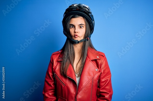 Young beautiful brunette motorcycliste woman wearing motorcycle helmet and jacket making fish face with lips, crazy and comical gesture. Funny expression. © Krakenimages.com