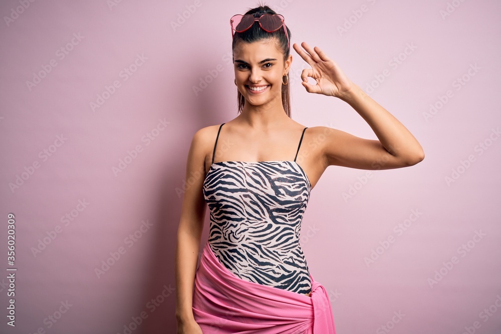 Φωτογραφία Young beautiful brunette woman on vacation wearing swimsuit over pink background smiling positive doing ok sign with hand and fingers