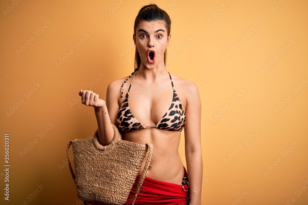 Φωτογραφία Young beautiful brunette woman on vacation wearing swimsuit and bag over yellow